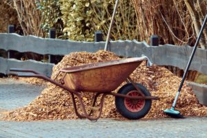 A wheelbarrow and a pile of mulch by a road.
