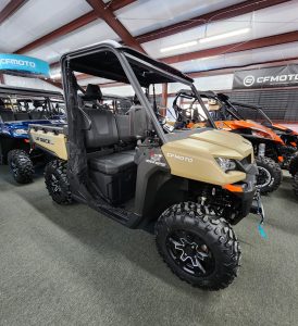 A tan 2024 UForce 1000 side by side UTV in a showroom.